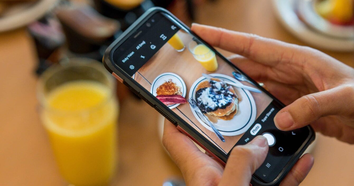 A girl captures a pancake with her mobile camera in hand.