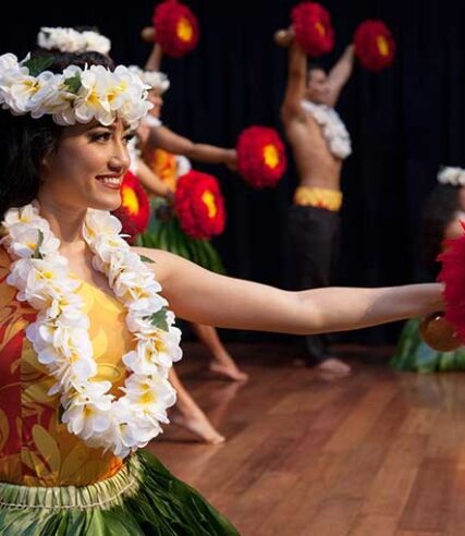 A girl adorned in flowers joyfully dances with a lively group.