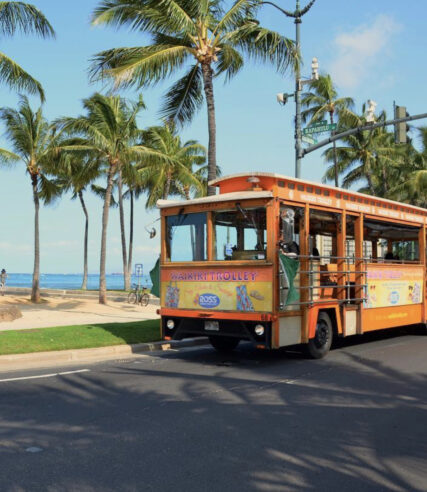 A Waikiki theme bus on the road near the beach.