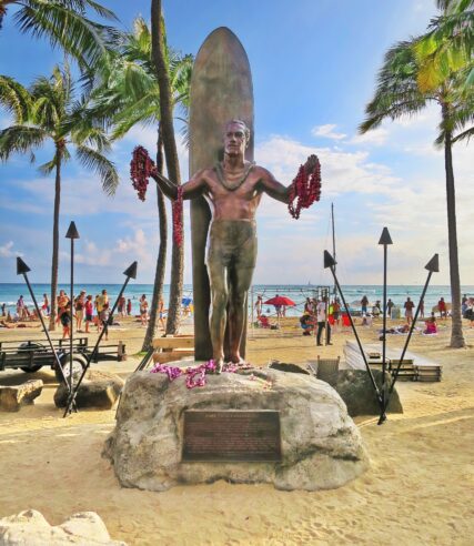 A statue of a man holding a surfboard on a beach