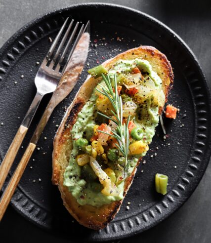 A black plate holds a vegetable-topped toast with a delightful presentation.
